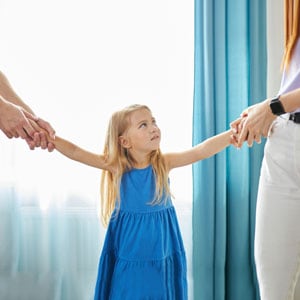 A child holding hands with two adults, representing child custody. - Law Office of Jordana N. Better