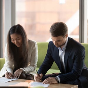 Two business professionals engaged in signing legal documents at a table, discussing California law on prenups and postnups - Law Office of Jordana N. Better